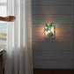 Mellow Monkey stained glass hummingbird nightlight glowing on a wall next to a window with sheer curtains