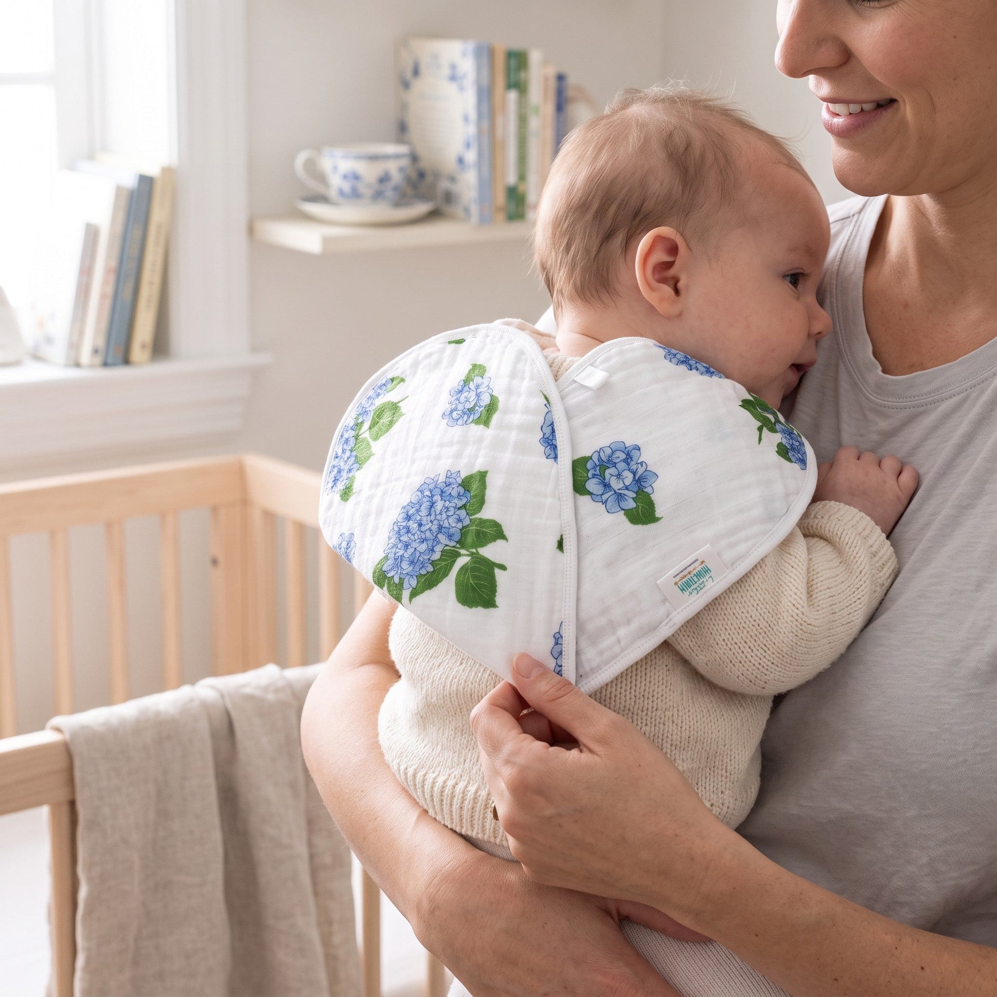 Mellow Monkey 2-in-1 bamboo and cotton muslin burp cloth and bib featuring a blue hydrangea floral print on a baby.