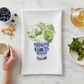 Mellow Monkey white cotton flour sack towel featuring a blue and white vase with green hydrangeas on a marble table.