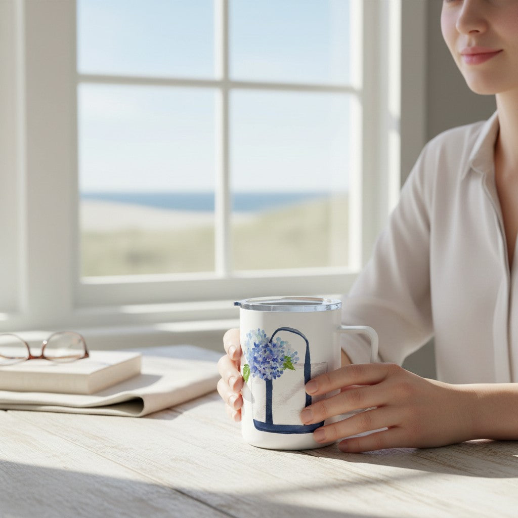 Mellow Monkey 12oz insulated stainless steel mug with blue hydrangea floral art held by a woman at a sunny table.