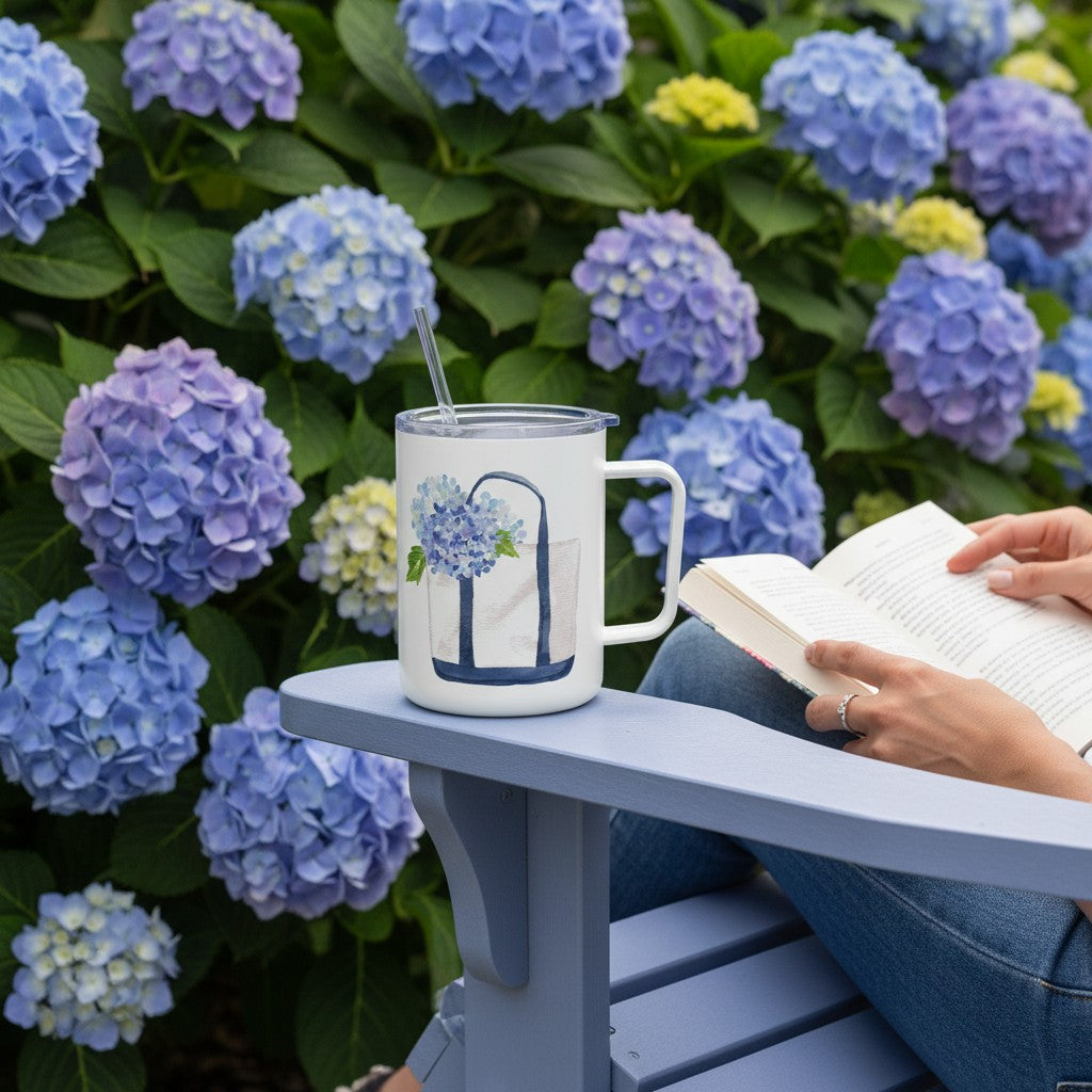 Mellow Monkey 12oz stainless steel insulated mug with hydrangea tote print, sitting on a chair by blue hydrangeas.