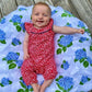 Mellow Monkey hydrangea print muslin swaddle blanket with a smiling baby in a red floral romper lying on top