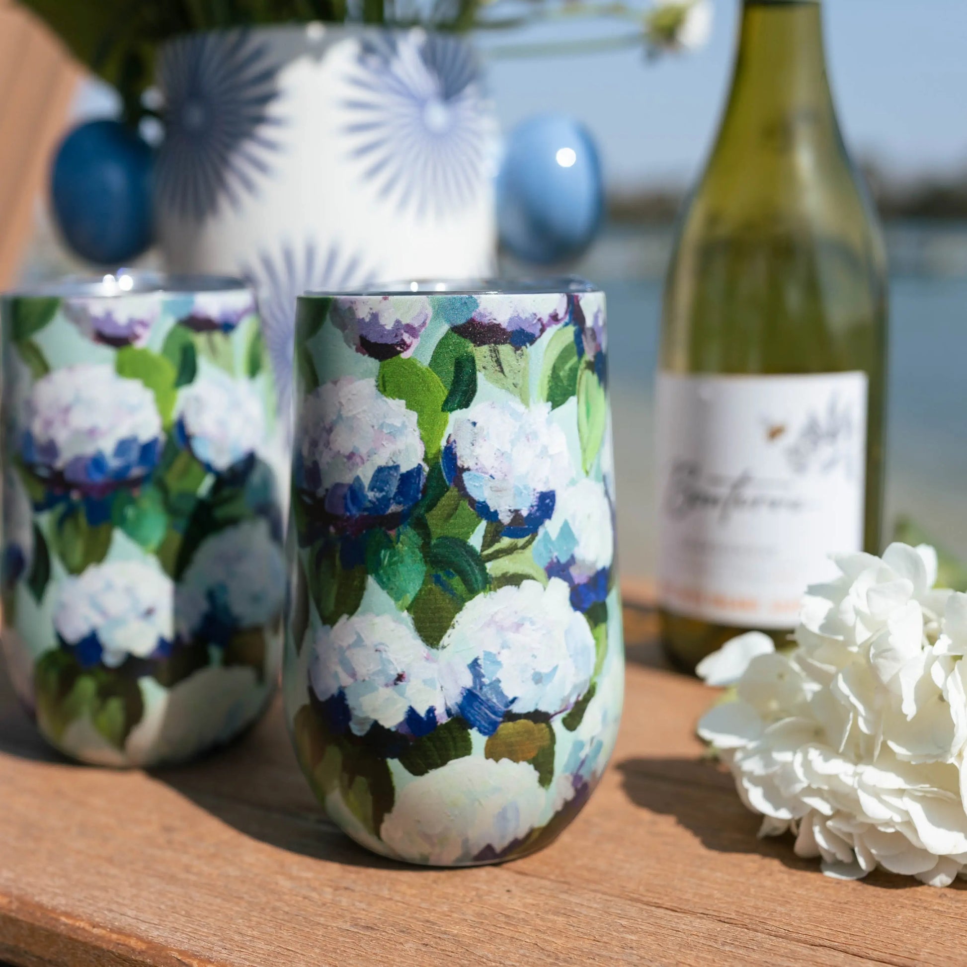 Mellow Monkey 16oz stainless steel wine tumbler with a blue and white coastal hydrangea floral print on a wooden table