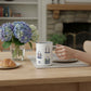 Mellow Monkey 12oz insulated stainless steel mug with summer tote bag print, held by a hand on a wooden table.