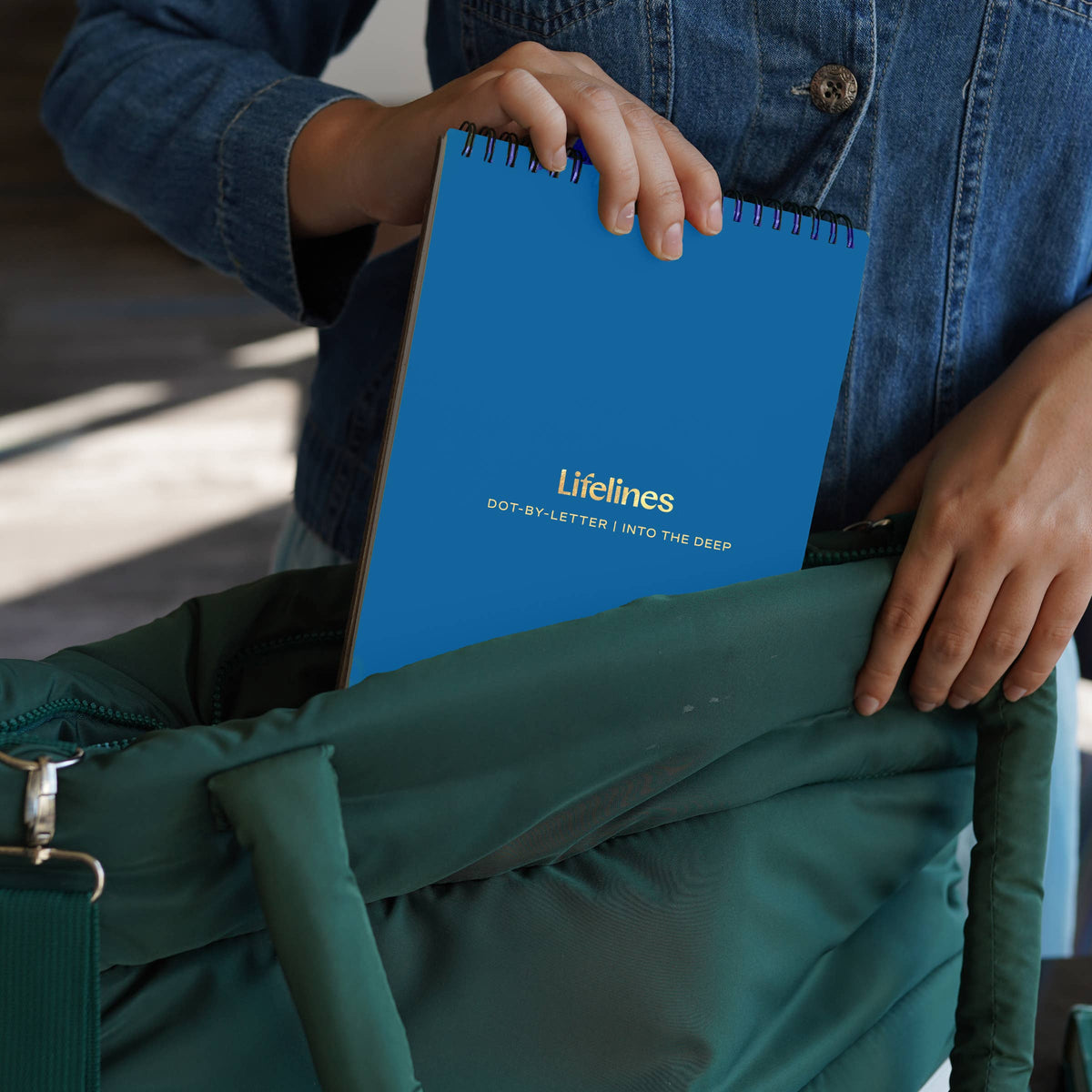 Mellow Monkey Into the Deep dot-by-letter activity book being placed into a dark green tote bag by a person.