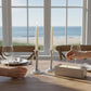 Mellow Monkey ivory 7-inch taper candles burning in silver holders on a dining table overlooking the ocean