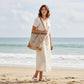 Woman carrying a Mellow Monkey Quirky Hues jute and canvas tote bag with leather accents on a sunny beach.