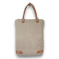 Mellow Monkey beige organic jute tote bag with brown leather handles and reinforced base corners.