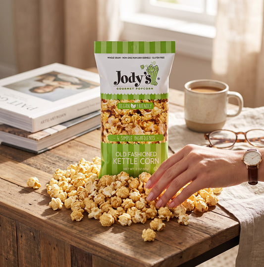 Mellow Monkey Jody's Old Fashioned Kettle Corn bag on a wooden table with a hand reaching for the popcorn snack