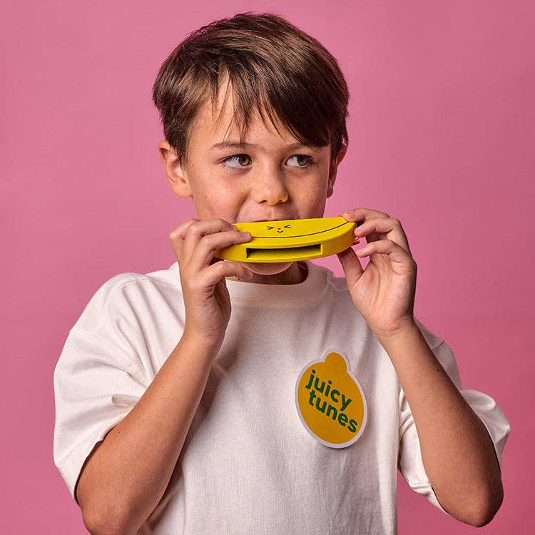 Mellow Monkey Kidoki wooden banana harmonica held by a young boy against a pink background