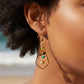 Mellow Monkey kite-shaped dangle earrings with colorful beads worn by a woman on a sunny beach.