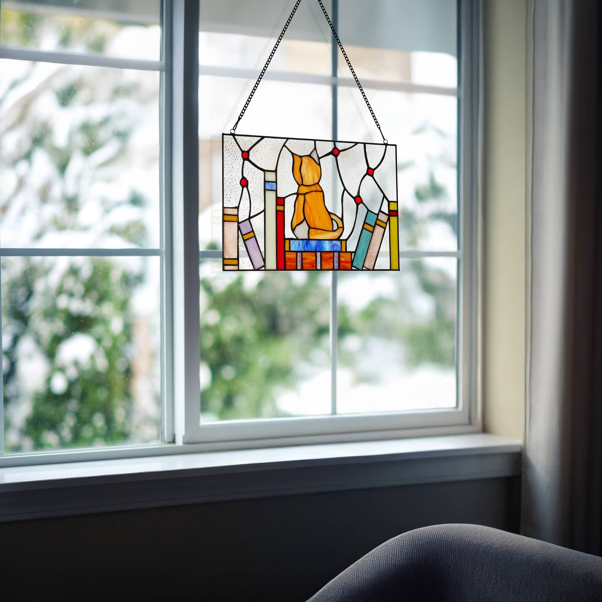 Mellow Monkey stained glass window panel featuring an orange kitten sitting on colorful books, hanging in a window.