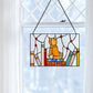 Mellow Monkey stained glass window panel featuring an orange kitten sitting on a stack of books in a bright window.