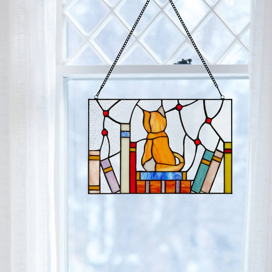 Mellow Monkey stained glass window panel featuring an orange kitten sitting on a stack of books in a bright window.