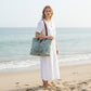 Woman in white dress carrying a Mellow Monkey La Couspaude canvas and leather tote bag on a sandy beach.