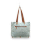Mellow Monkey La Couspaude canvas tote bag in light blue with brown leather handles and a zippered exterior pocket.