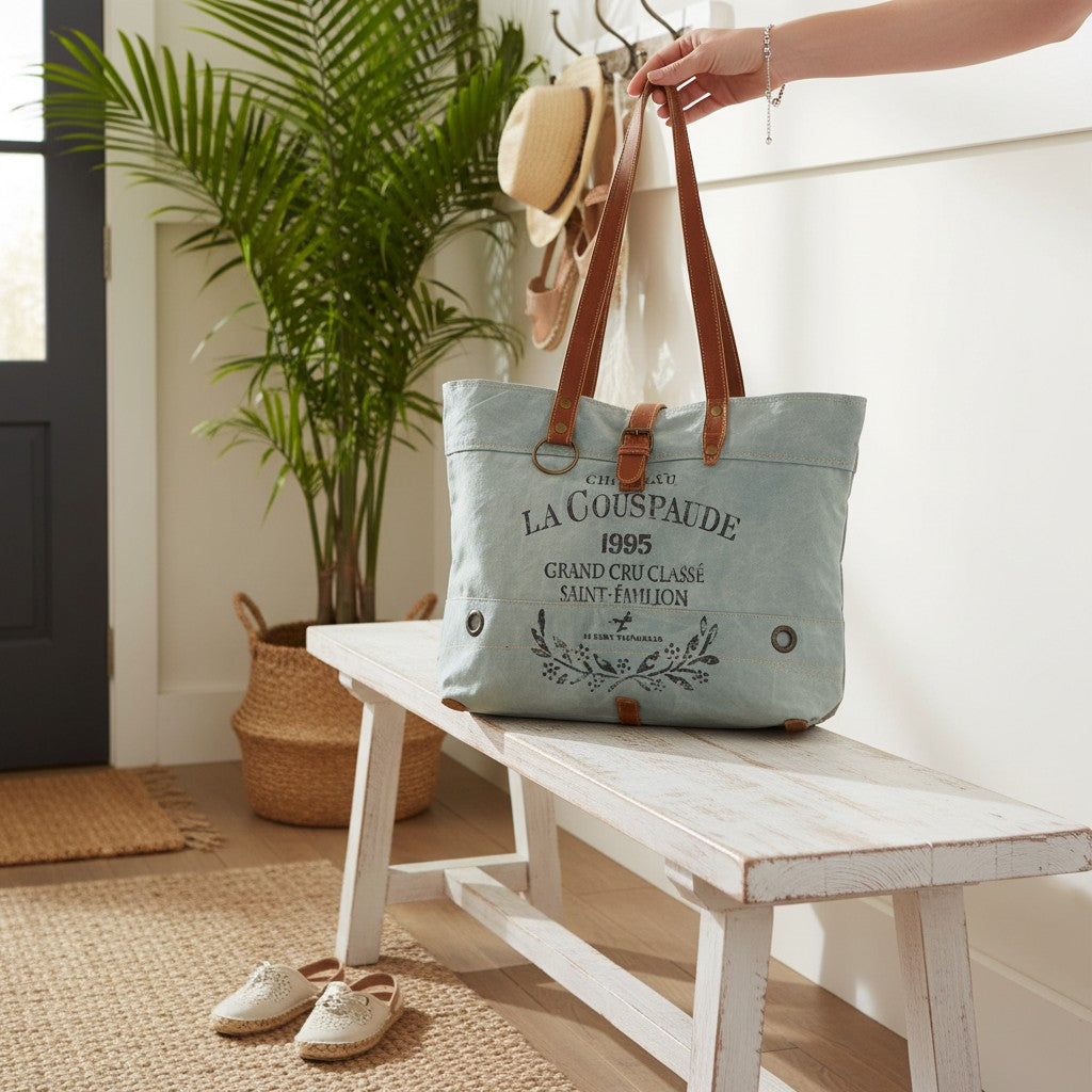 Mellow Monkey La Couspaude canvas tote bag with brown leather handles and vintage-style graphic print on a bench.