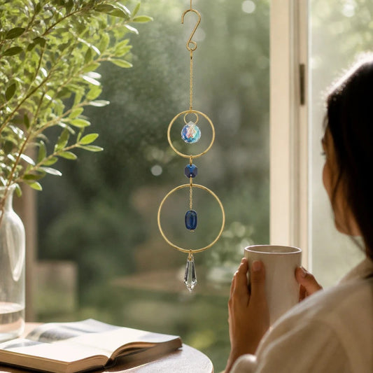 Mellow Monkey Lapiz healing ornament suncatcher with blue crystals and bronze rings hanging in a sunlit window