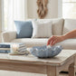 Mellow Monkey large dusty blue ceramic shell bowl on a wooden coffee table with a hand placing a small shell inside.