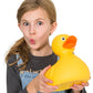 A young girl holding a large yellow Mellow Monkey plastic bath duck toy with a playful expression.
