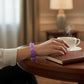 Mellow Monkey Lavender Sparkle Feelzies sensory bracelet worn on a wrist next to a steaming cup of coffee and a book.