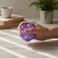 Mellow Monkey Lavender Sparkle Feelzies sensory bracelet being squeezed by a hand on a marble table.