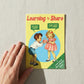 Mellow Monkey "Learning To Share" birthday card featuring a retro illustration of a boy offering a cake to a girl who says "FUCK OFF! IT'S MINE!"
