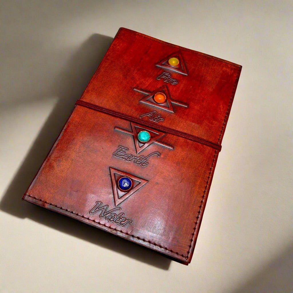 Mellow Monkey reddish-brown leather journal with elemental symbols (Fire, Air, Earth, Water) and gemstone accents, secured by a cord closure.