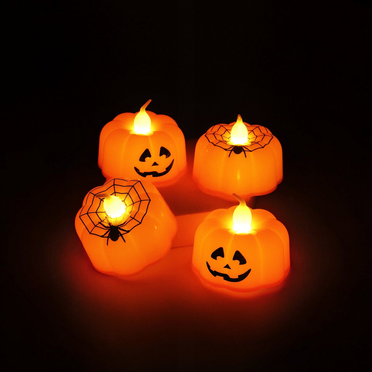 Mellow Monkey set of four orange plastic LED pumpkin jack-o'-lantern tealights with spiderweb and face designs.