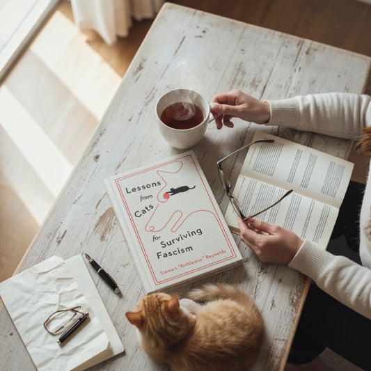 Mellow Monkey Lessons from Cats for Surviving Fascism hardcover book on a rustic table with a cat and coffee