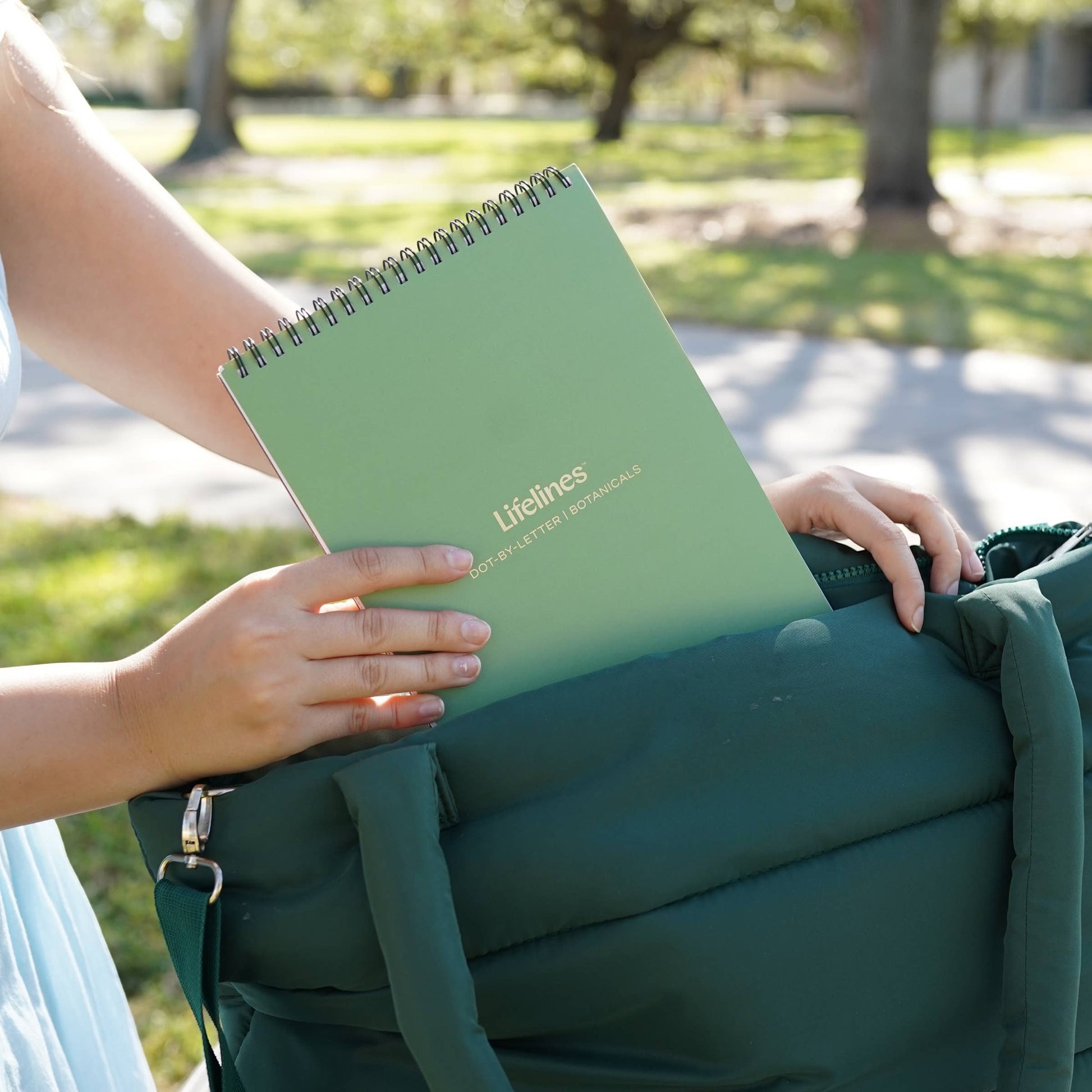 Mellow Monkey Lifelines FlowArt trace-to-doodle pad with a sage green cover being placed into a dark green tote bag.