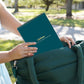 Mellow Monkey Lifelines FlowArt trace-by-line pad in dark teal being placed into a matching green tote bag outdoors.