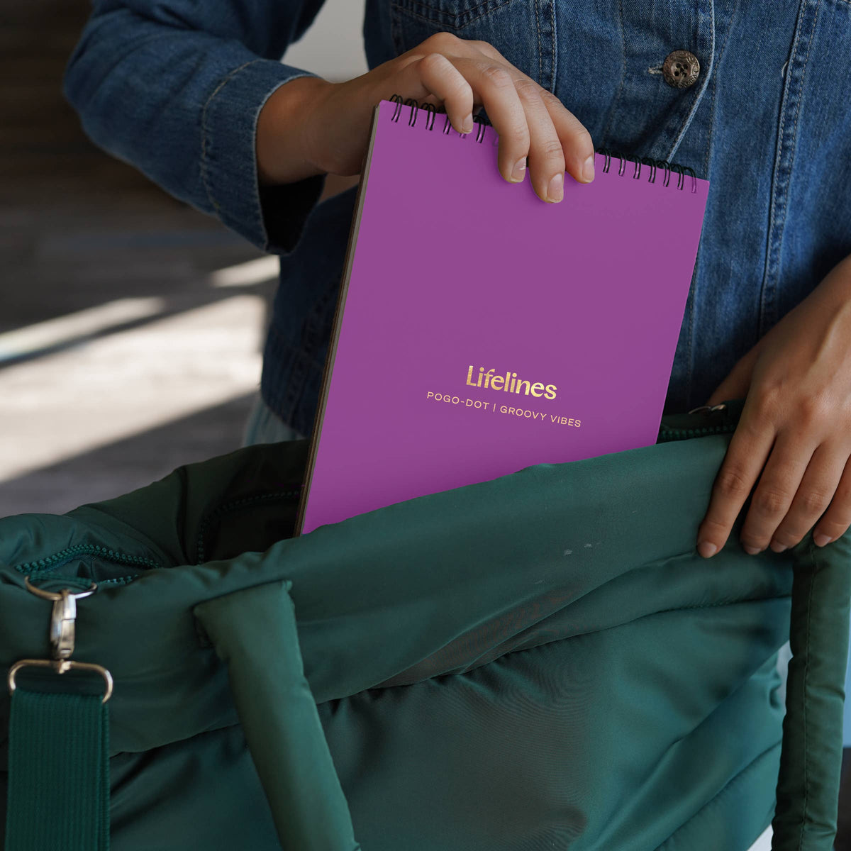 Mellow Monkey Lifelines Pogo-Dot Groovy Vibes purple spiral-bound art book being placed into a green tote bag