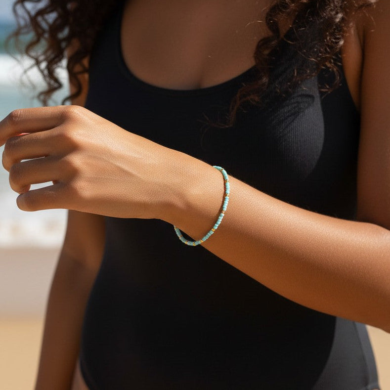 Mellow Monkey light blue seed bead bracelet with 18K gold plated accents worn by a woman on a sunny beach.
