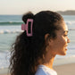 Mellow Monkey jumbo light pink matte rectangle hair claw worn by a woman on a sunny beach
