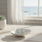 Mellow Monkey lighthouse earrings with blue crystals in a white shell dish on a table by a beach window.
