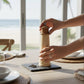 Mellow Monkey lighthouse shaped salt and pepper mill, 8-inch, made of rubberwood, on a table with peppercorns.