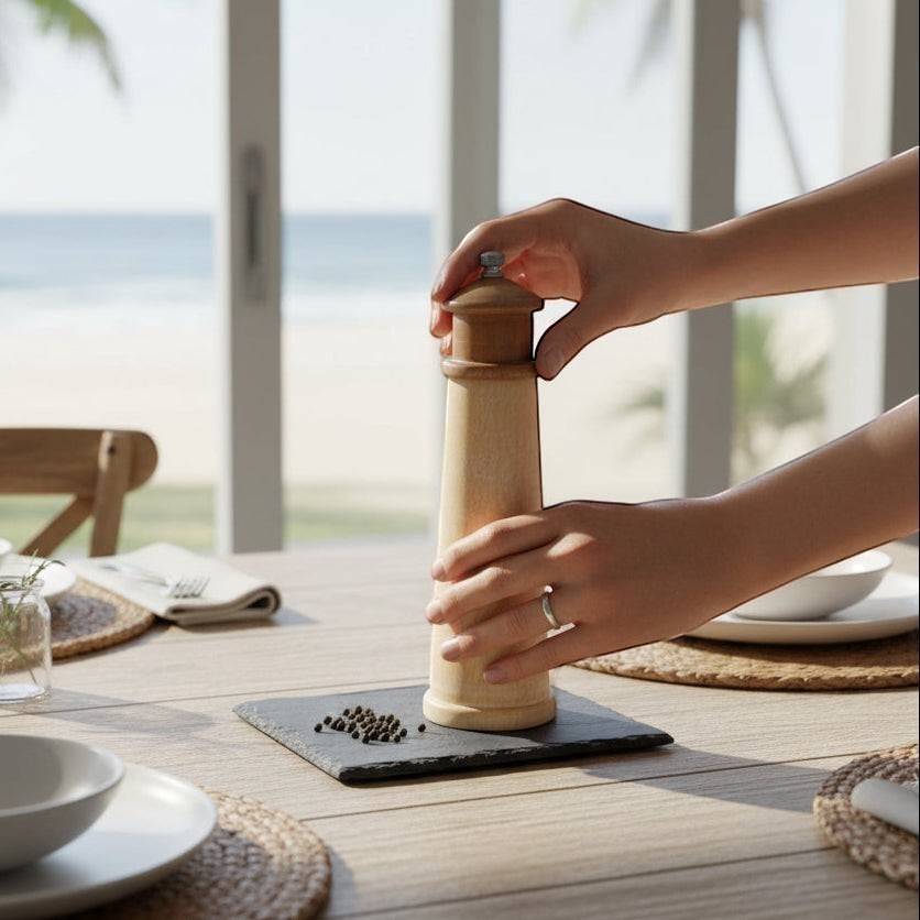Mellow Monkey lighthouse shaped salt and pepper mill, 8-inch, made of rubberwood, on a table with peppercorns.