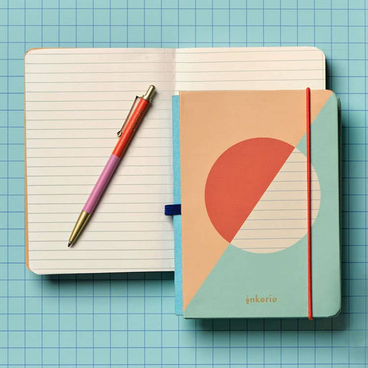 Mellow Monkey lined mini notebook with a matching multi-colored pen on a blue grid background