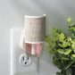 Mellow Monkey Linen WallScents fragrance warmer plugged into a wall outlet with a pink oil refill