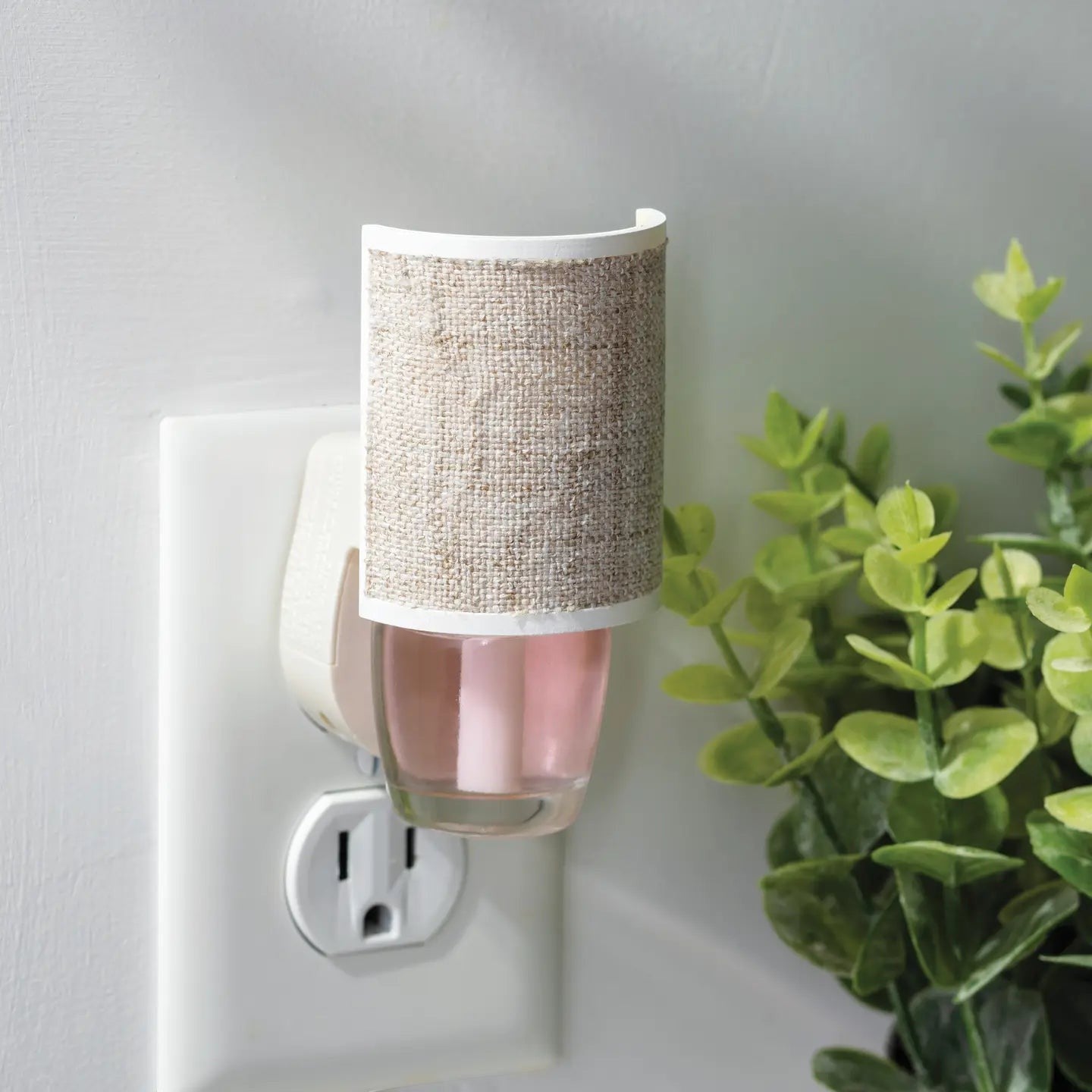 Mellow Monkey Linen WallScents fragrance warmer plugged into a wall outlet with a pink oil refill