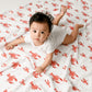 Mellow Monkey baby lying on a white muslin swaddle blanket with a red lobster print pattern