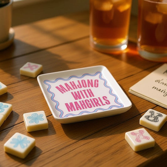 Mellow Monkey ceramic Mahjong With Mahgirls trinket tray with pink and blue text on a wooden table with game tiles.