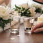 Mellow Monkey set of 2 clear shot glasses with gold lettering: "Maid of Honor" and "Best Man" with a black bow tie graphic.
