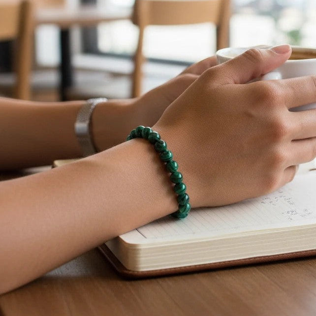 Mellow Monkey malachite synthetic stone beaded bracelet on a person holding a coffee cup at a desk.