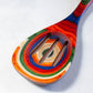 Mellow Monkey Marrakesh Collection wooden slotted spoon with colorful swirls of red, orange, blue, green, and white.