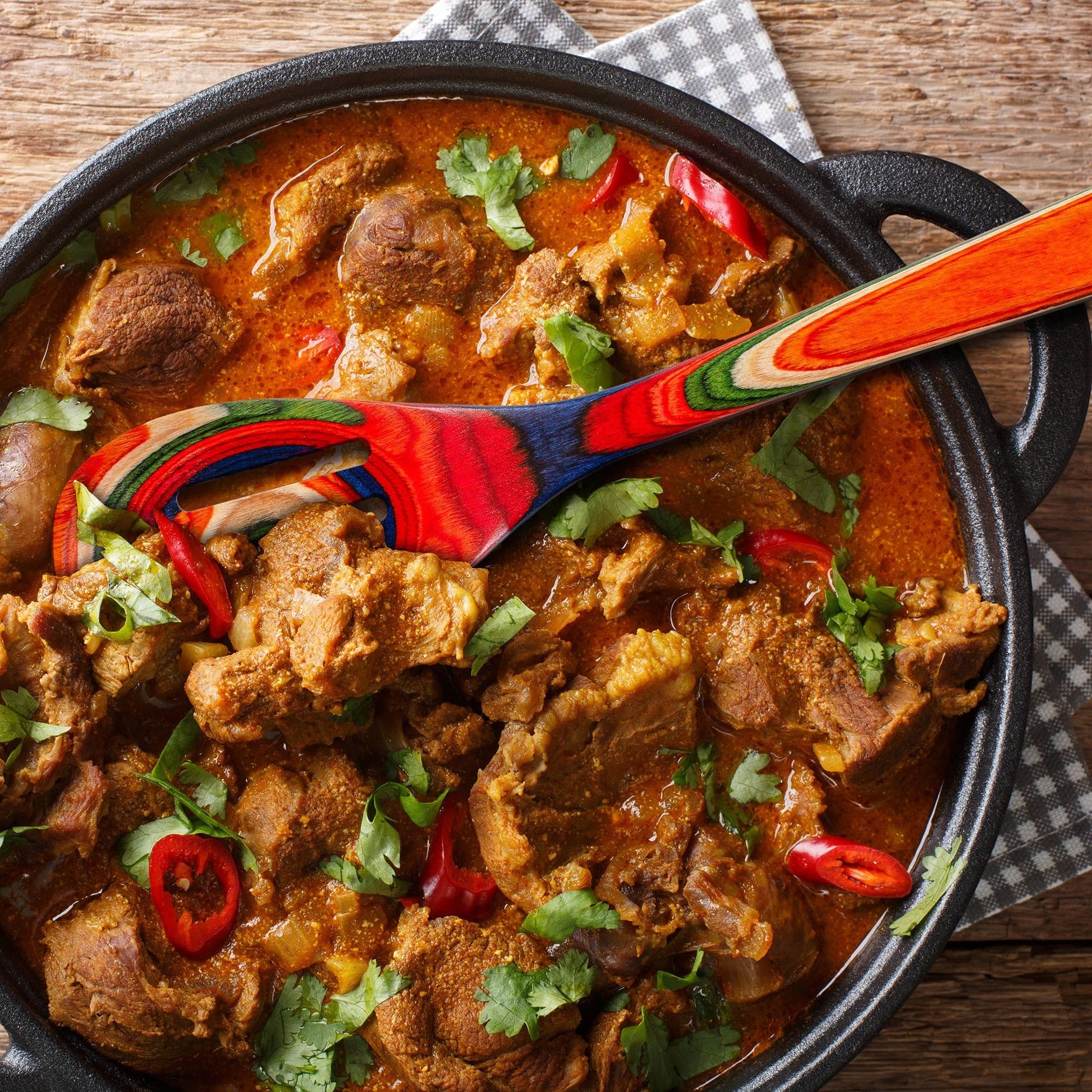Mellow Monkey Marrakesh Collection wooden slotted spoon with colorful swirl design, 12-1/2-in, stirring a pot of lamb curry.