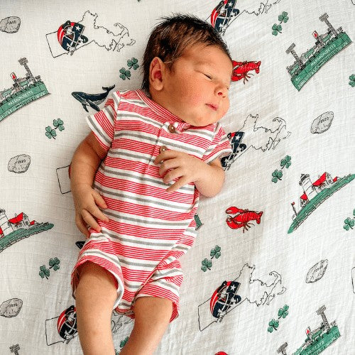 Newborn baby sleeping on a Mellow Monkey Massachusetts themed muslin swaddle blanket with state icons and symbols.