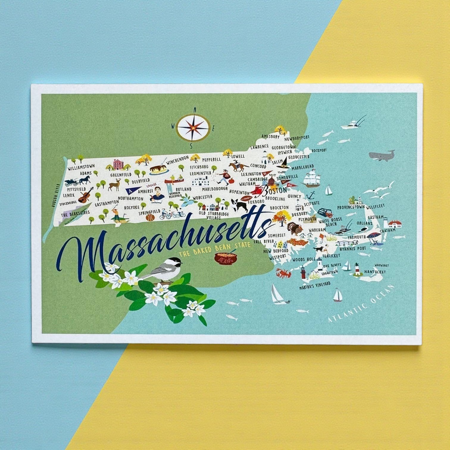Mellow Monkey Massachusetts postcard map with illustrations of towns, landmarks, and wildlife. Features a chickadee bird and flowers.