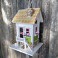 Mellow Monkey May Cottage birdhouse with white exterior, pink door and windows, flower boxes, and stone accents.